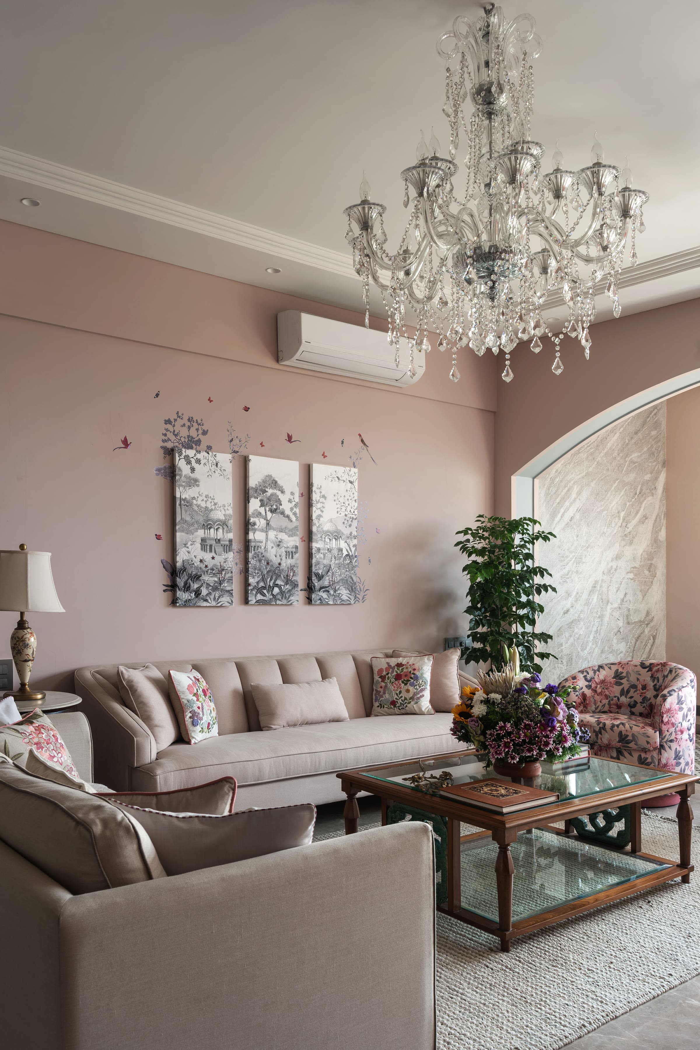 A living room with a long pale sofa beneath a triptych of botanical prints, a tall plant and a floral armchair alongside.