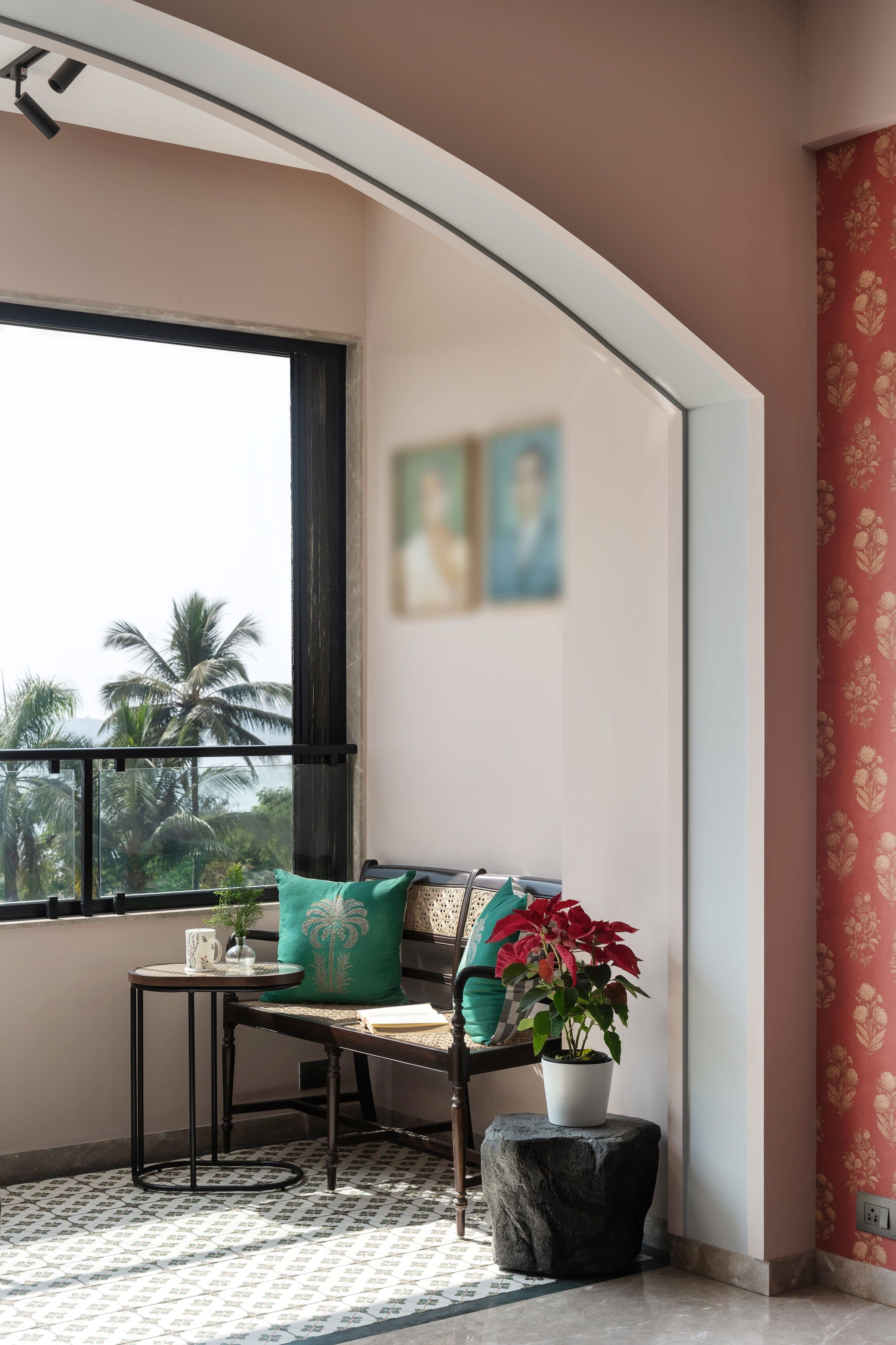 A corner seat by a tall window with palms outside, framed family portraits on the wall above and a poinsettia on the floor.