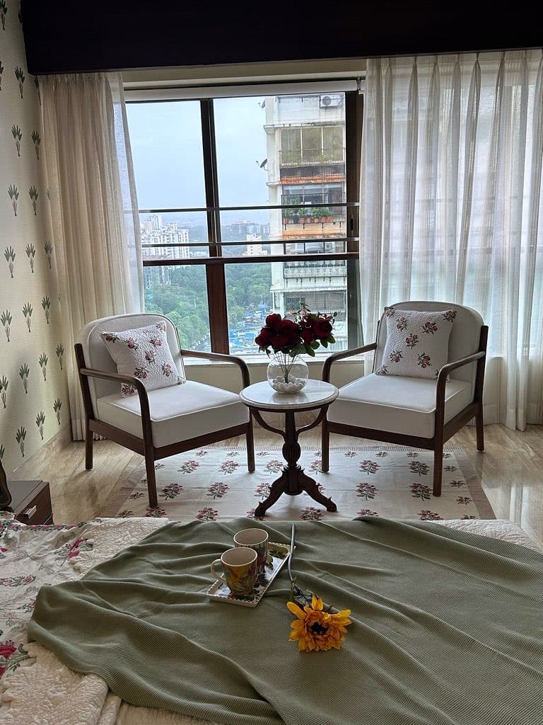 Two timber armchairs either side of a small pedestal table, drawn up to a window with the city beyond.