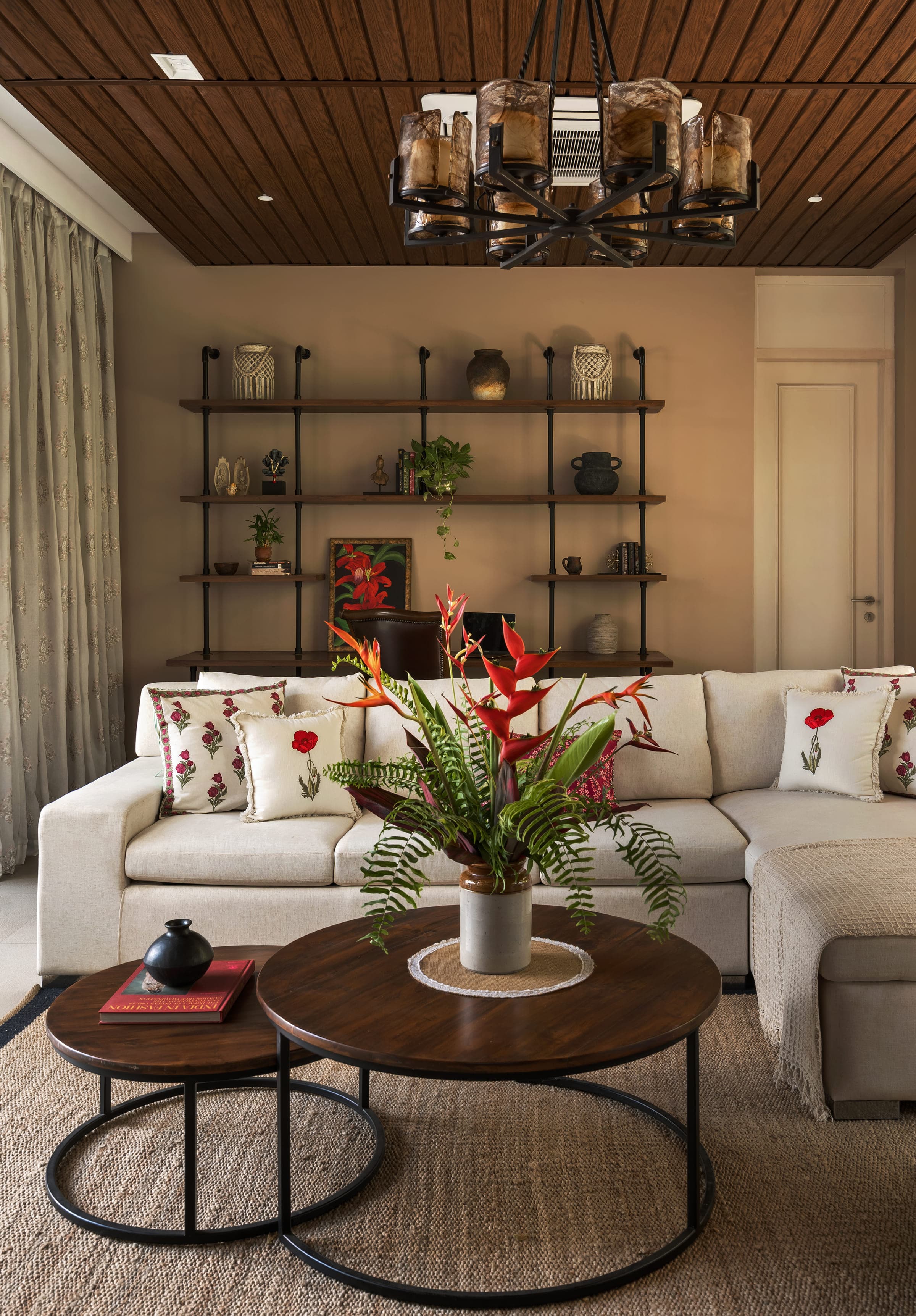 A corner of the living pavilion: a pale sectional sofa with block-printed cushions, a low table and flowering heliconia in a vase.
