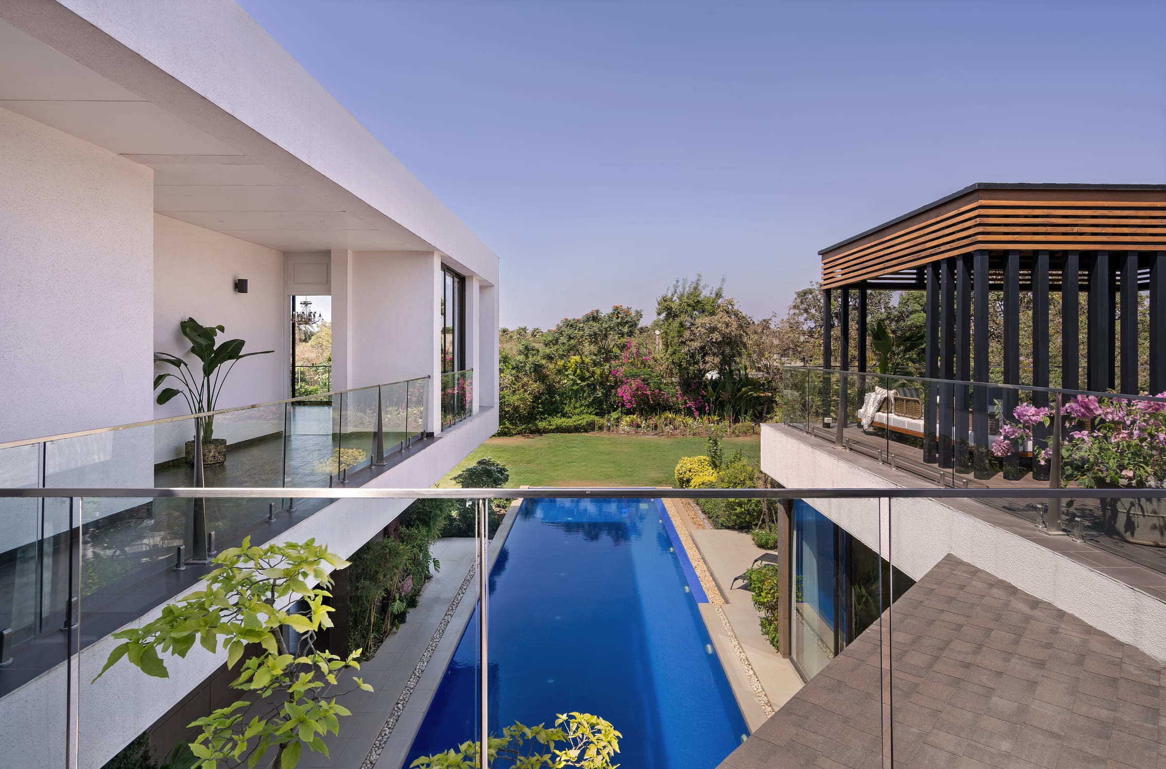 The length of the pool running beside the house, the timber pergola on the roof above and lawn and planting on the far side.
