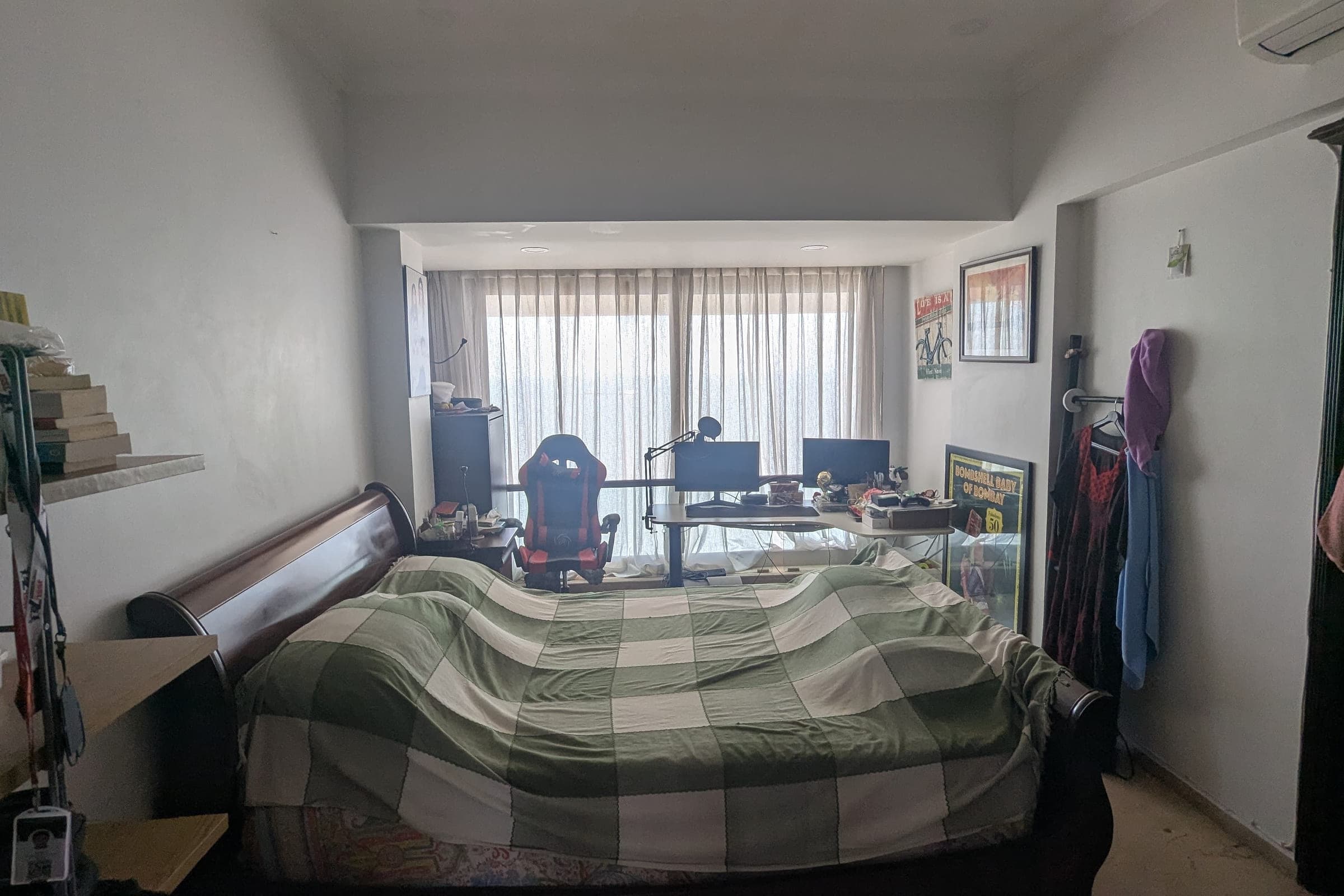The bedroom before the work: a checked bedspread, a desk and office chair under the window, shelving and clothes stacked along the walls.