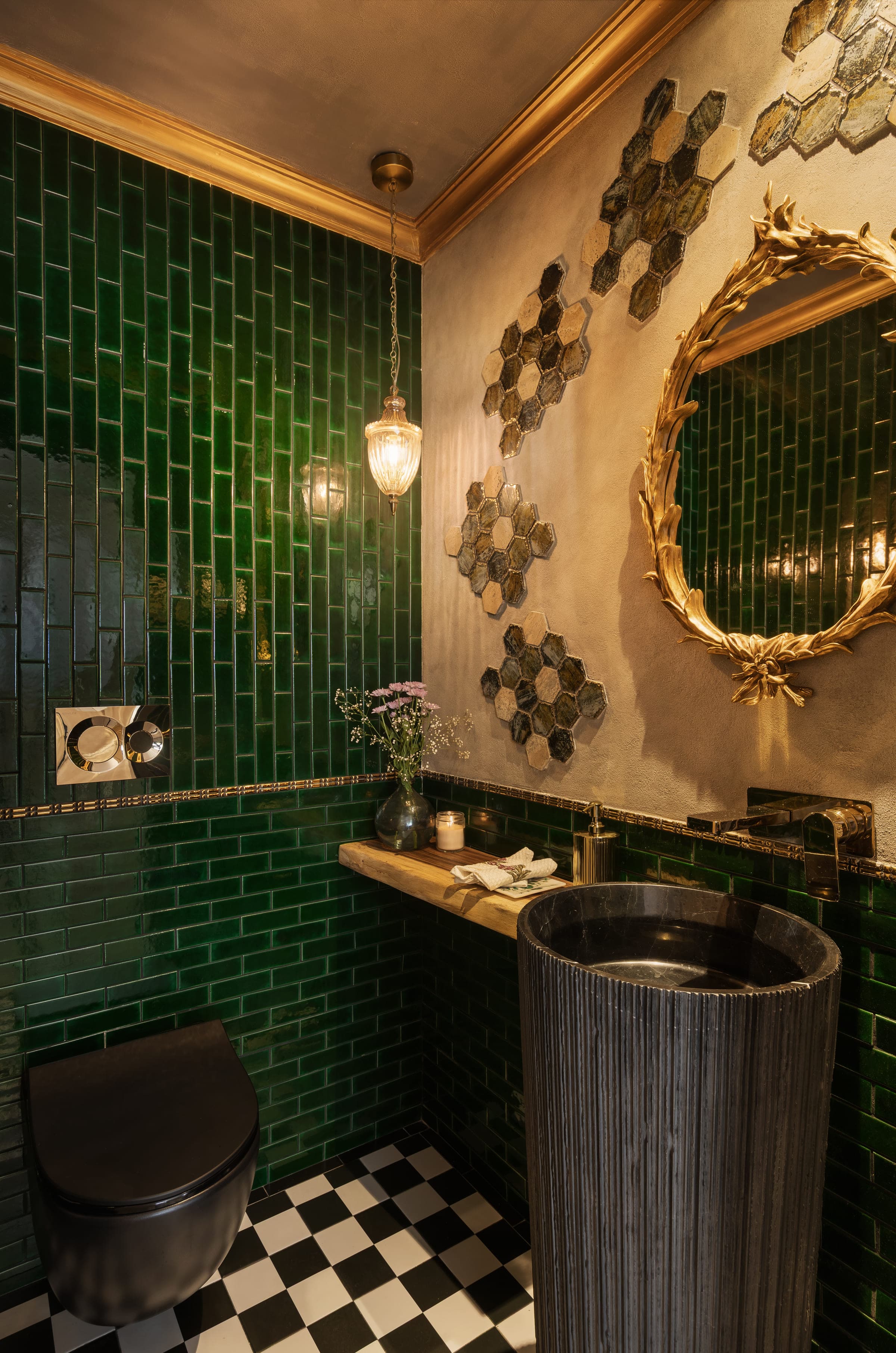 A bathroom lined in deep green tile with a gold-framed mirror, brass fittings and a hammered metal basin.