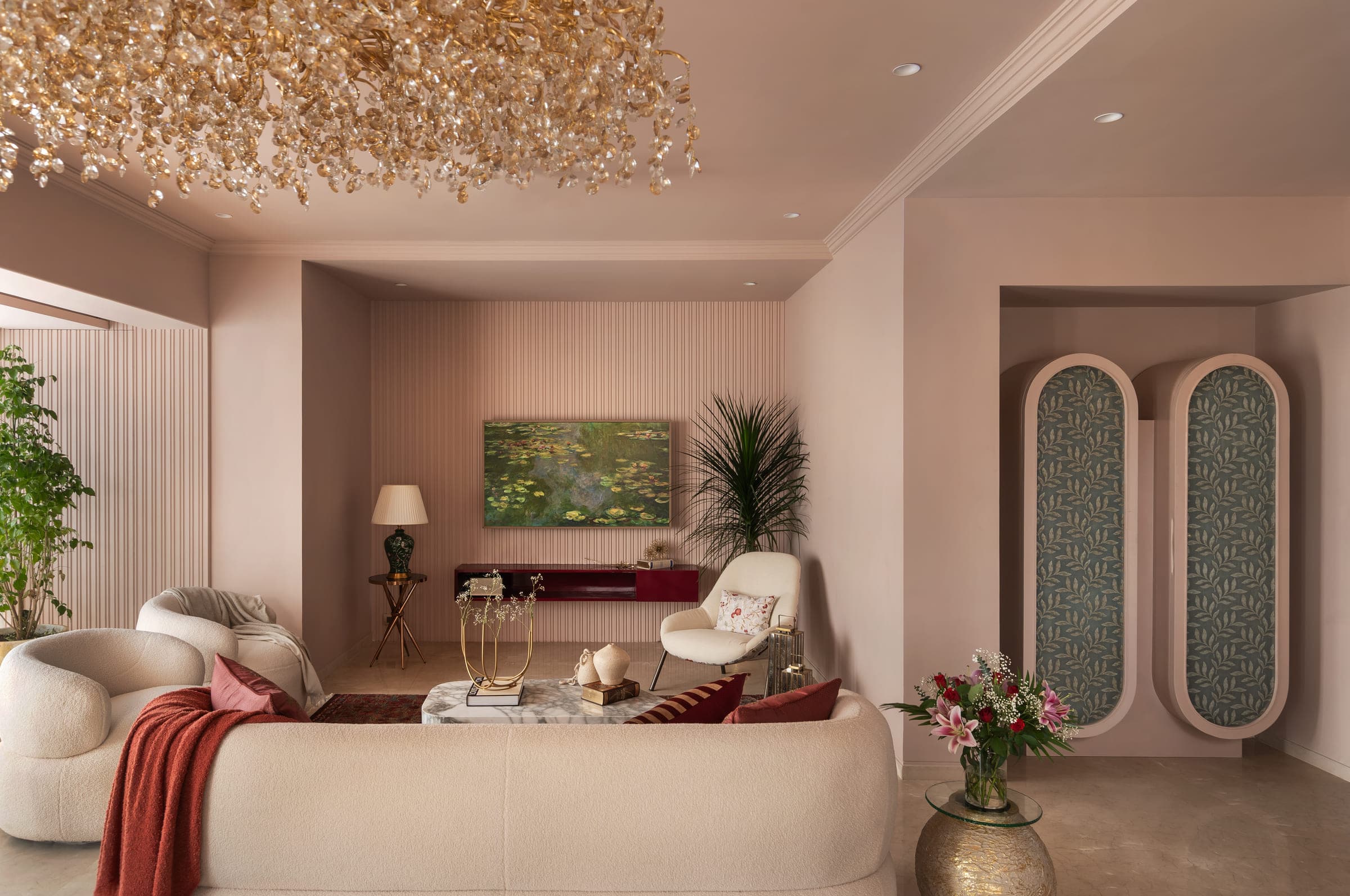 The living room late in the day, lamps lit, the curved seating and low burgundy console warm against the blush wall.