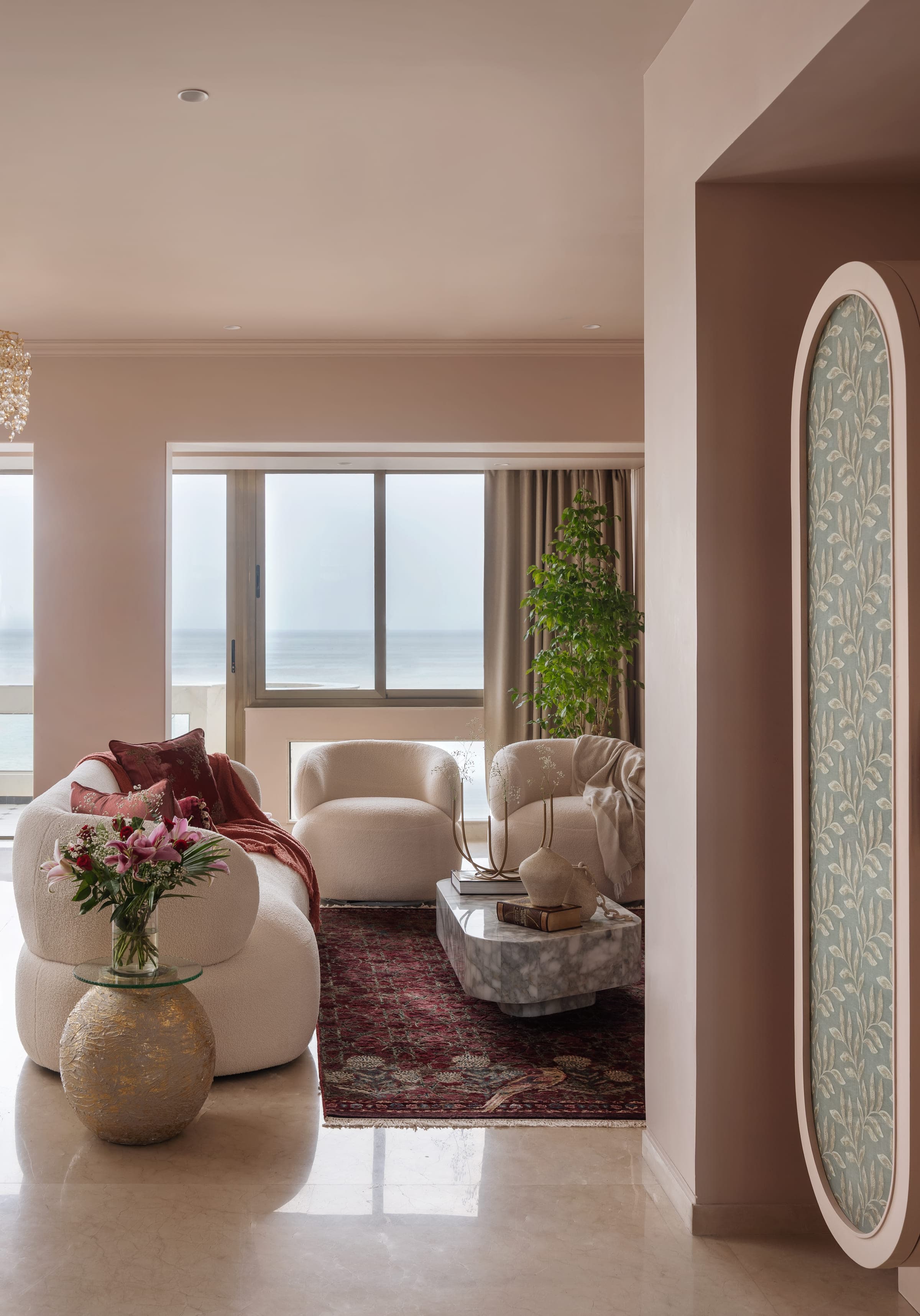 Curved cream armchairs and a low marble table in the living room, the sea filling the window behind them.