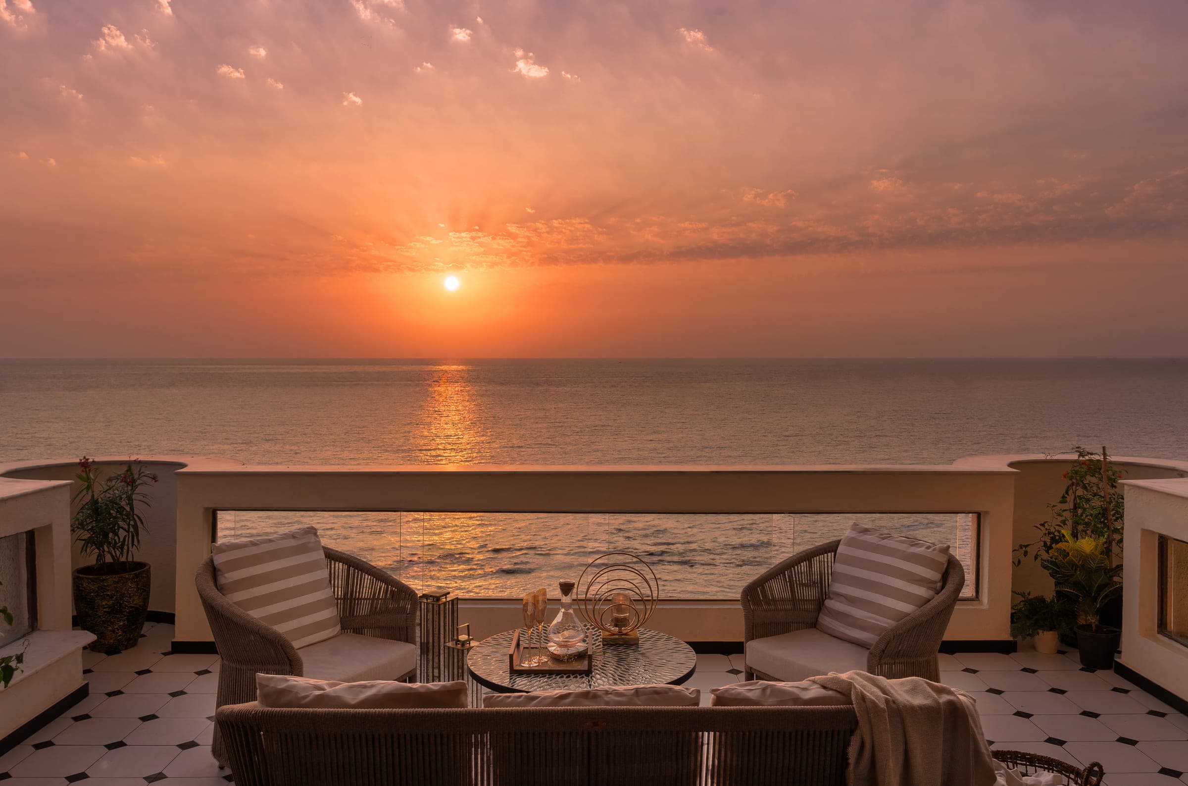 The terrace at sunset, cane seating and a low table arranged facing the sun as it drops into the sea.