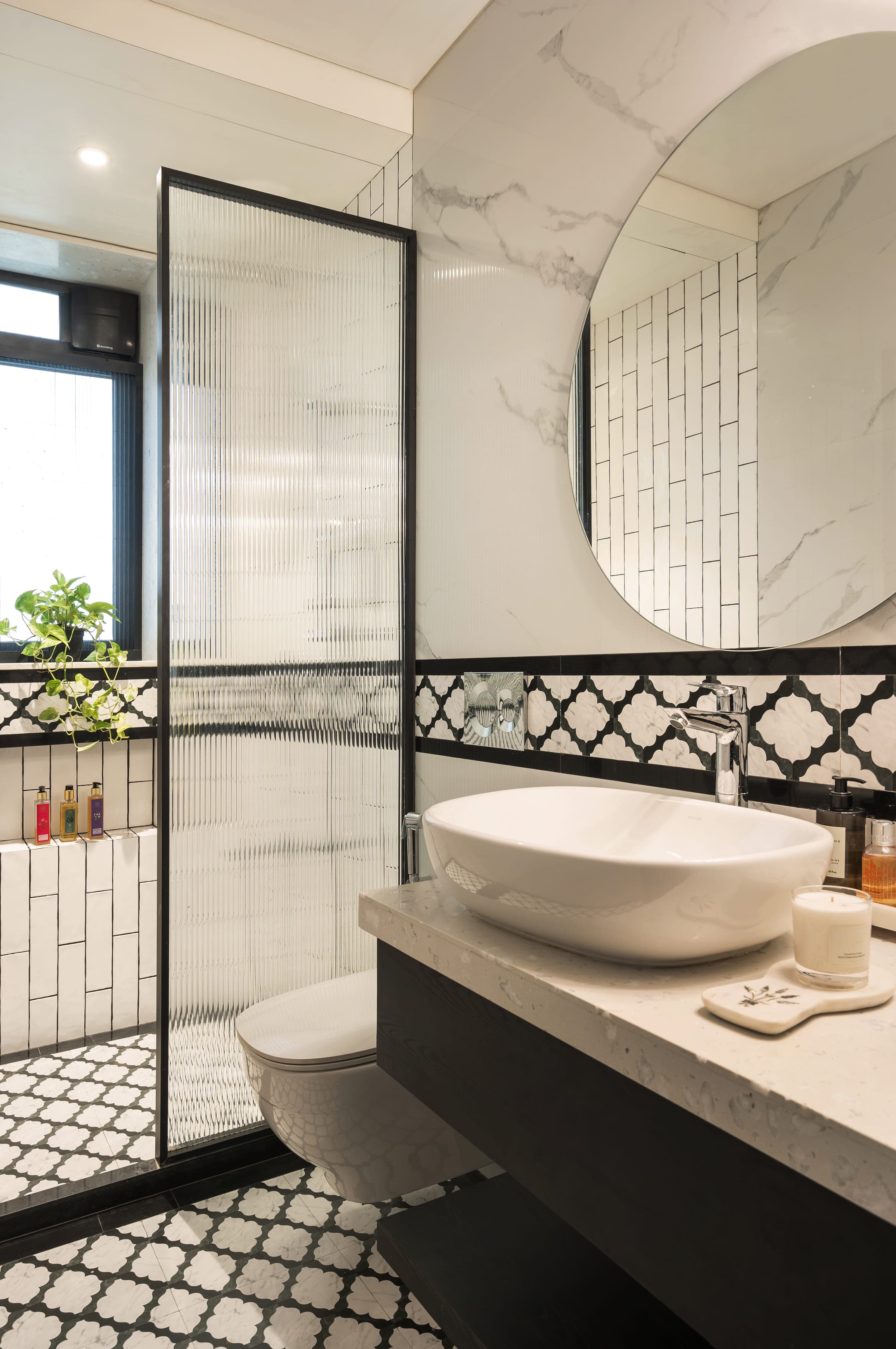 A second bathroom in white marble and small square tile, a black and white patterned floor, a round mirror above a stone basin and a reeded glass shower screen.