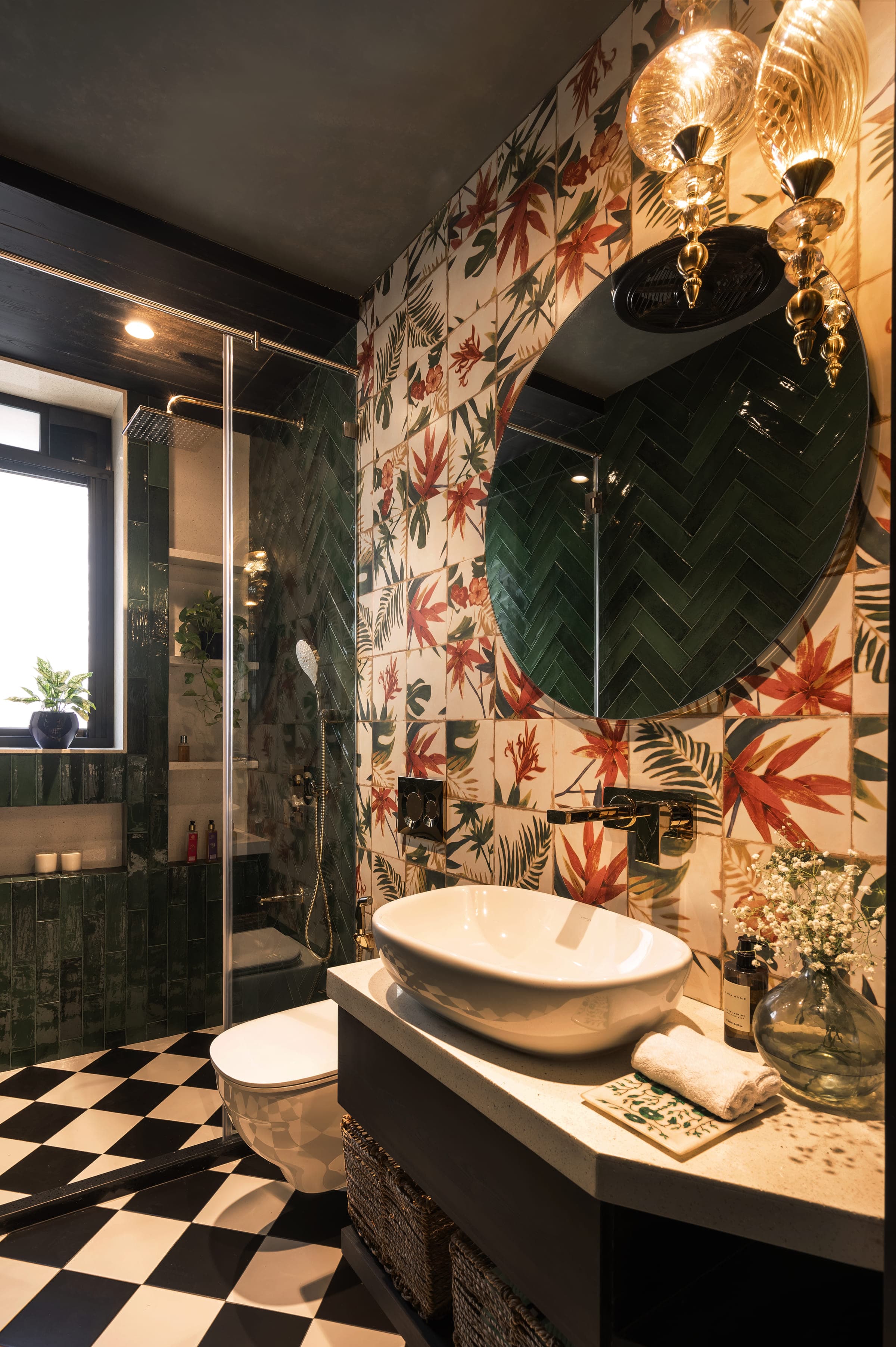 A bathroom tiled in dark green herringbone with a botanical print to one wall, a round mirror and a white basin.