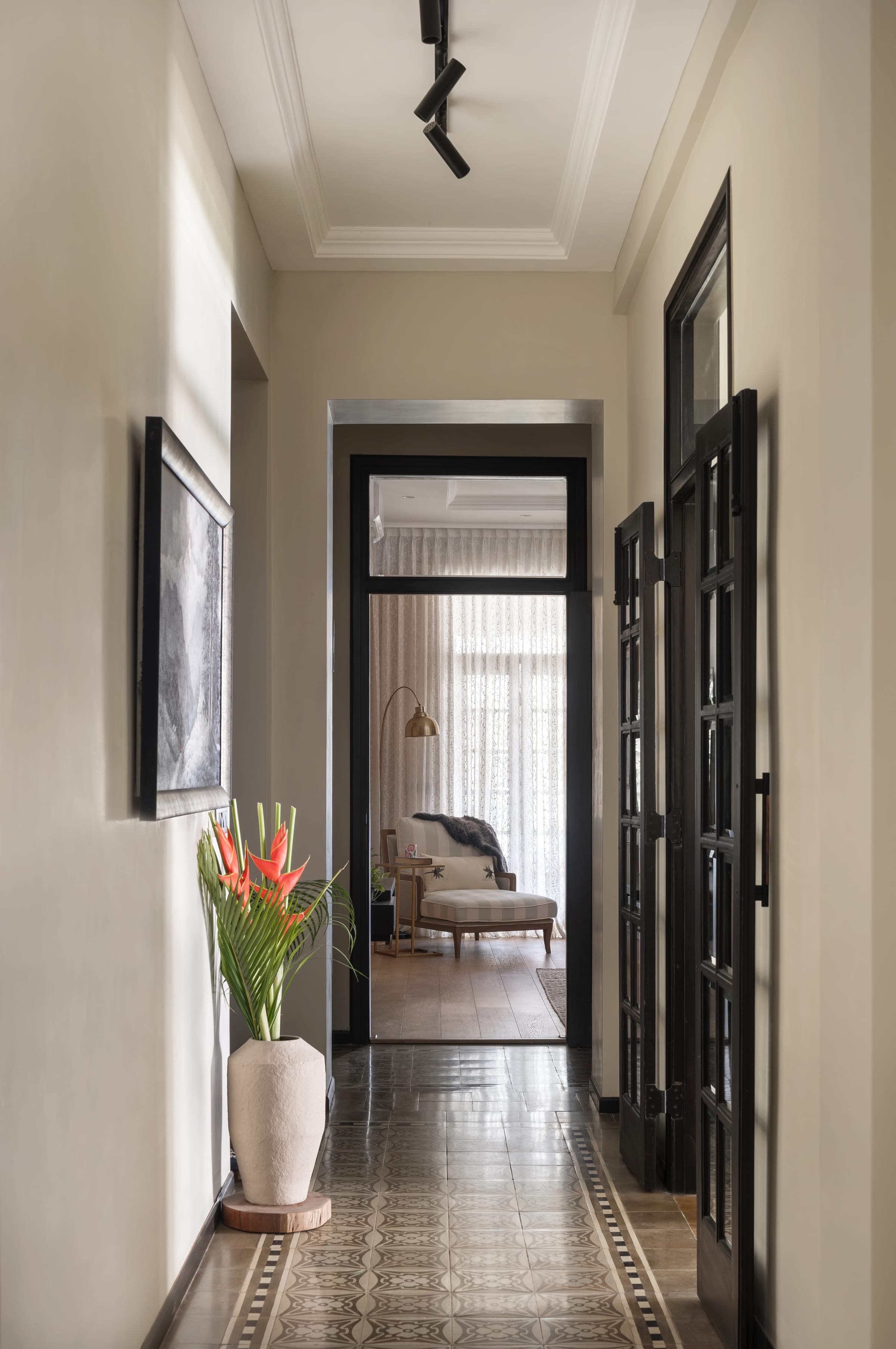 The corridor: patterned cement tile laid with a border running the length of it, black timber doors on both sides, a framed drawing and a tall vase of heliconia.
