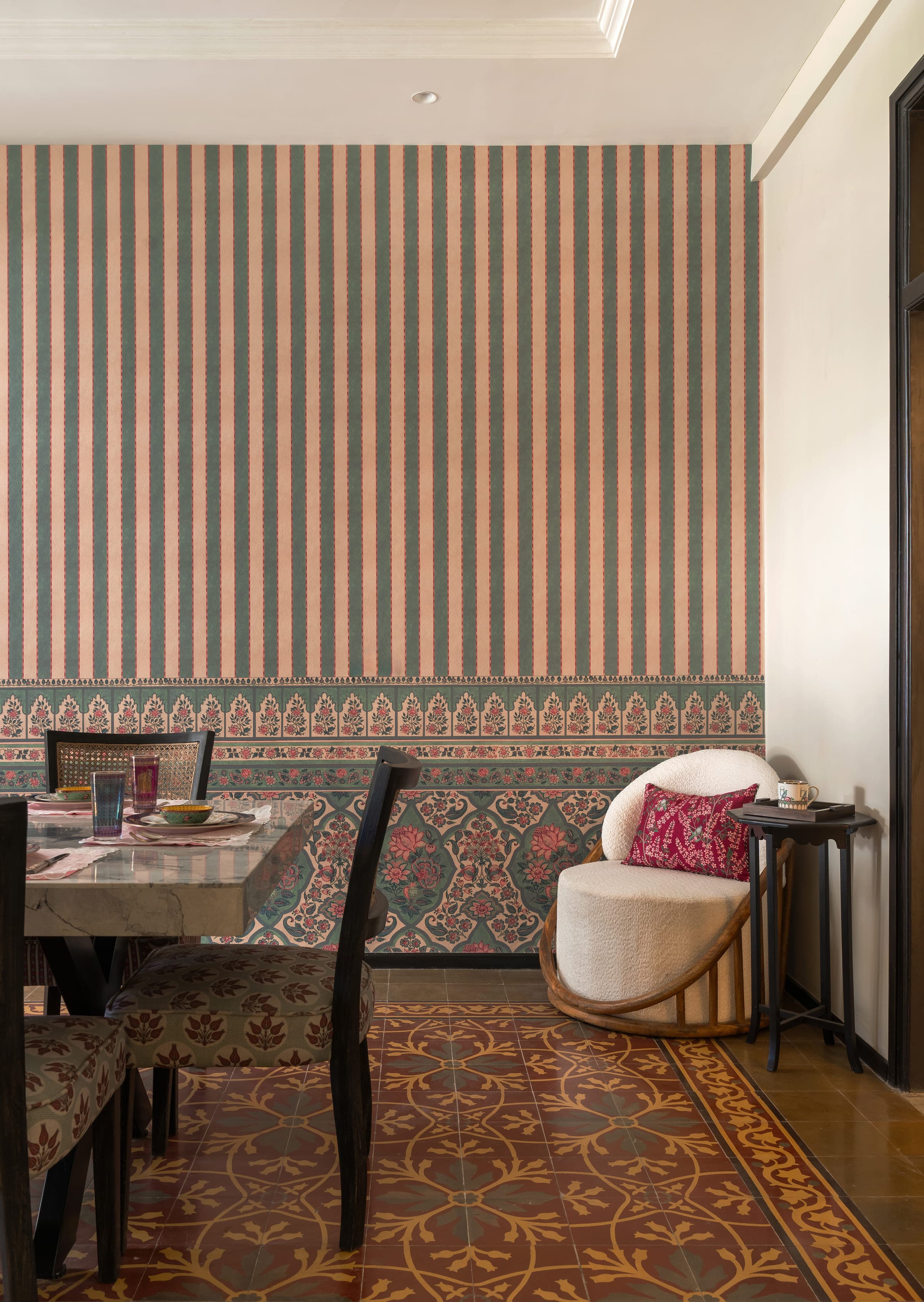 The seating corner of the dining room: a boucle tub chair with a bandhani cushion against the papered wall, a small tray table with a teacup beside it, and the marble table just in frame.