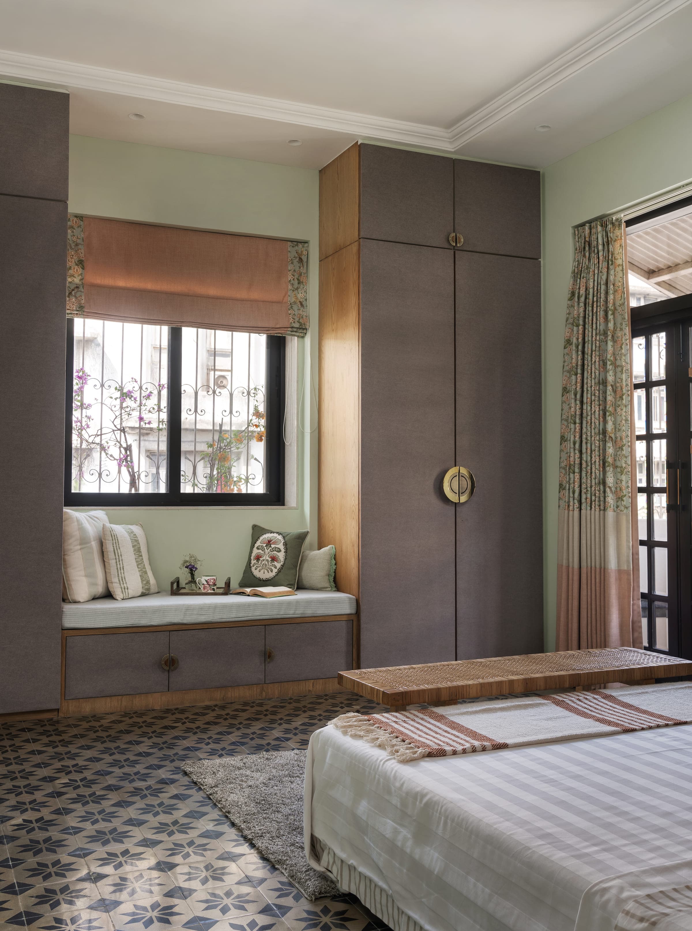 A cushioned window seat built into a bay, a bamboo blind half drawn and cupboards in soft grey to one side.