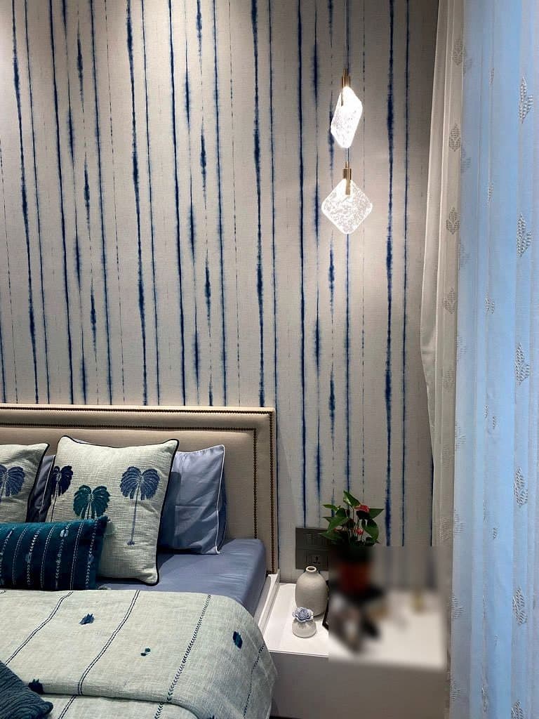 A faceted glass pendant hanging low beside the bed against the striped wall, a small plant and a framed picture on the bedside shelf.