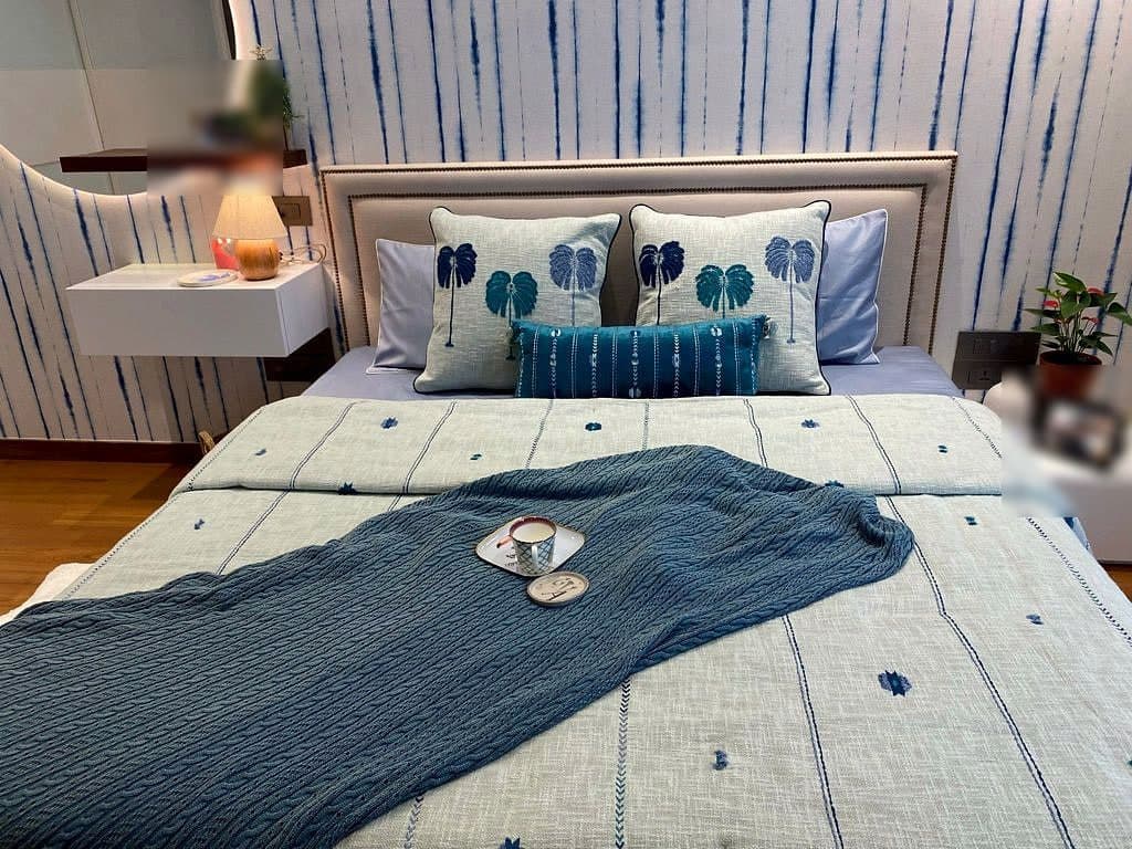 The bed made up in pale blue and white with a deep indigo throw folded across it and a tray set down on top.