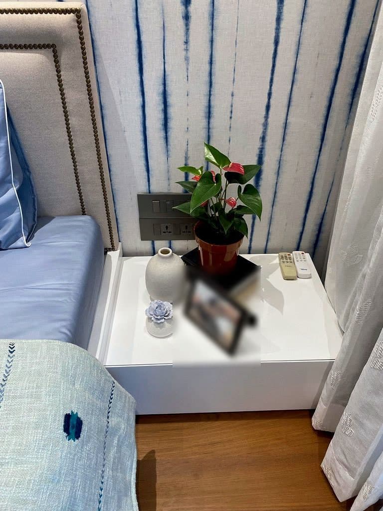 A floating white bedside table holding a potted anthurium, a small vase and a framed photograph, against the striped wall.