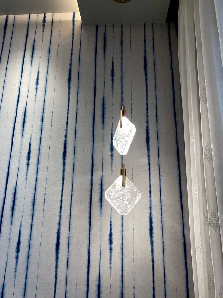 Two faceted glass pendants on a slim cord, hanging against the hand-dyed indigo stripes.