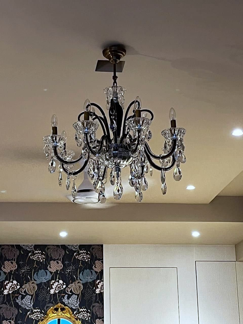 A crystal chandelier seen close against the ceiling, the dark floral wallpaper below it.