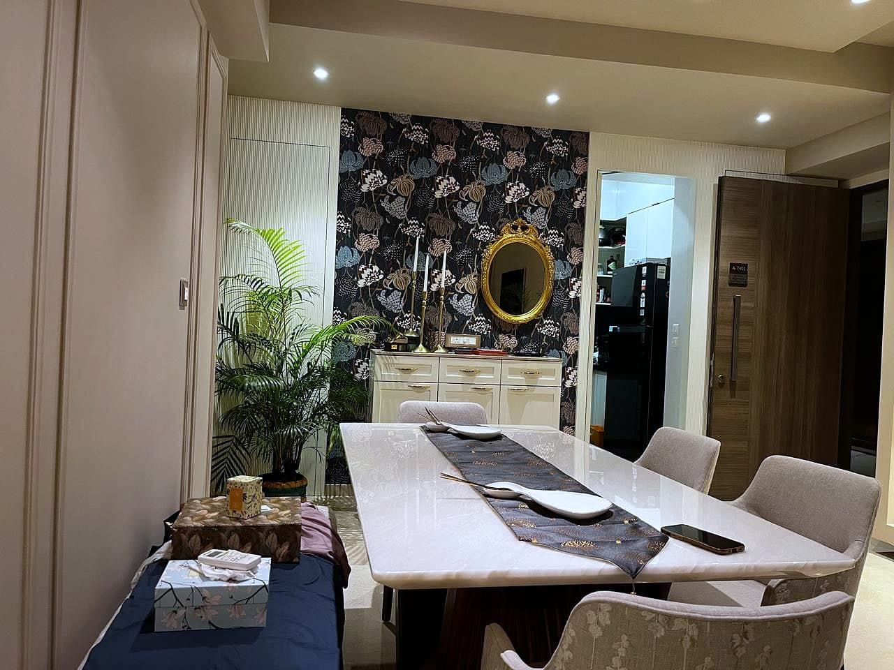 The dining table against the dark floral wall, an oval gilt mirror above a pale sideboard and a palm at the corner.