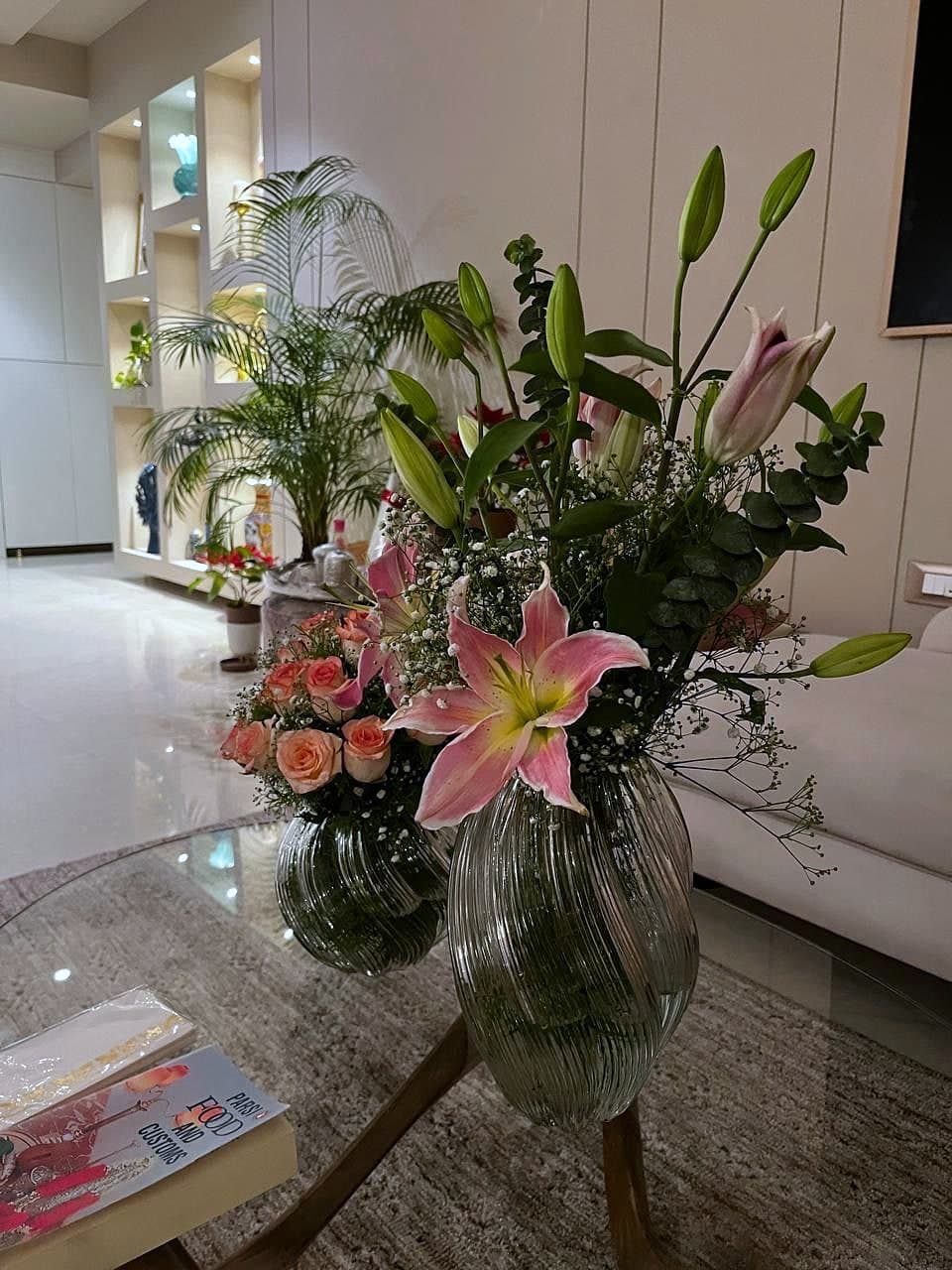 Cut lilies and roses in a glass vase on a marble surface, the room soft behind them.