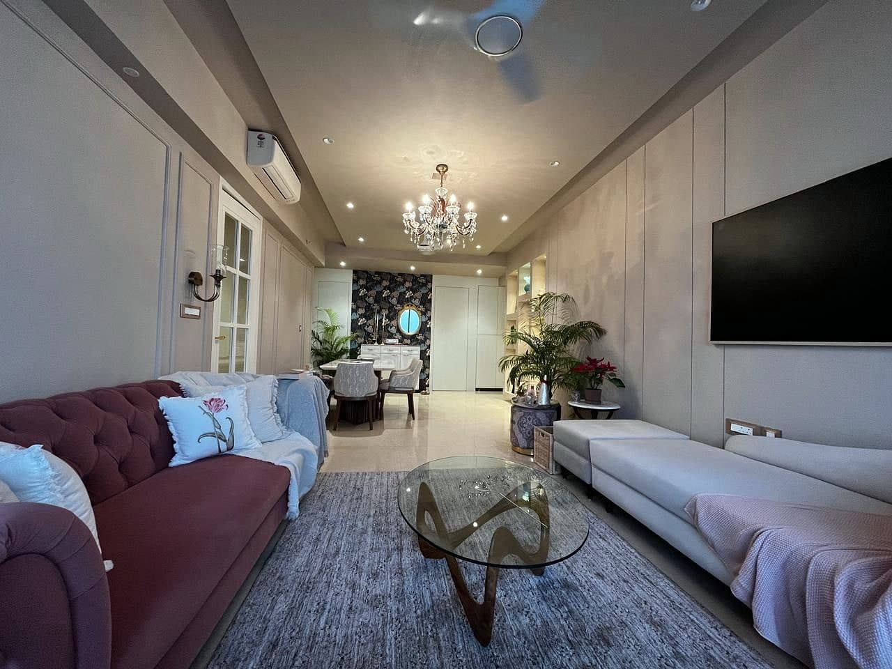 The living end seen wide, a burgundy sofa facing a cream one across a glass table, panelled walls and a chandelier above.