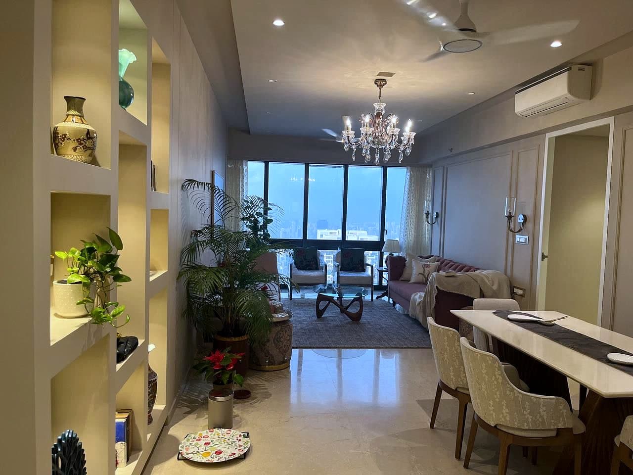 Backlit display niches holding pots and greenery, the length of the apartment visible past them to the window wall.